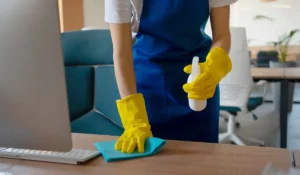Commercial cleaning services staff wiping and sanitizing office desk with cleaning spray and cloth.